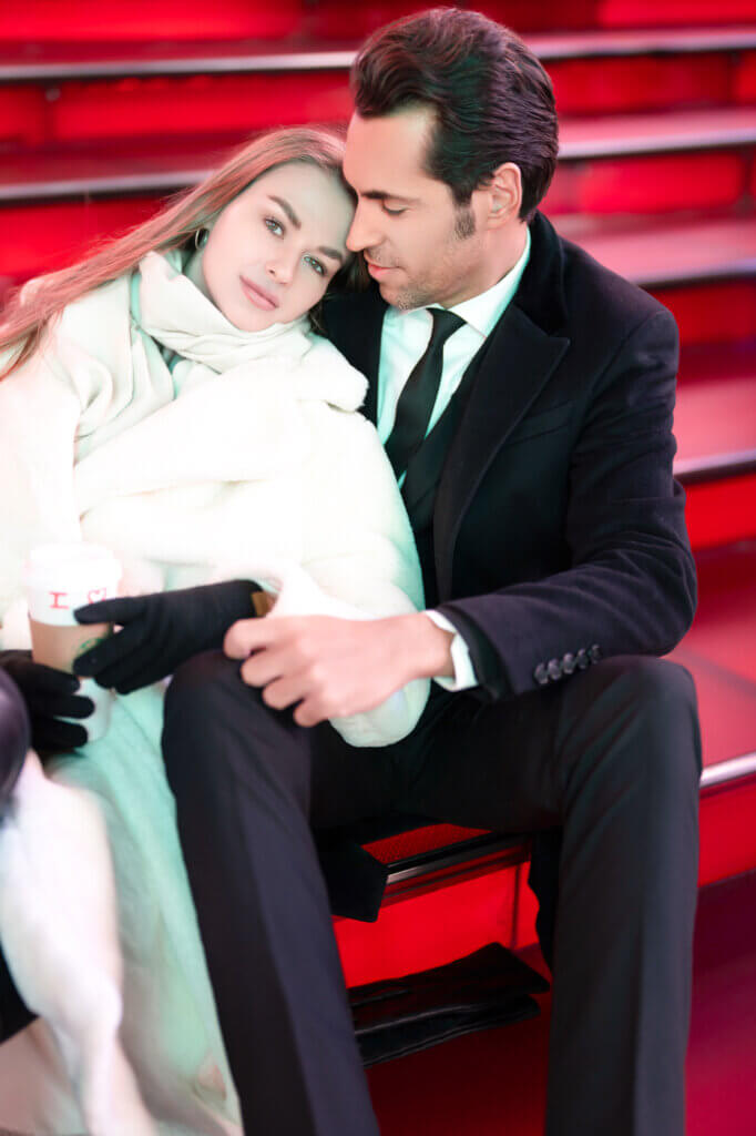 An elegant couple romantically embraces on the iconic red stairs at Times Square amidst the bright lights of the city that never sleeps.